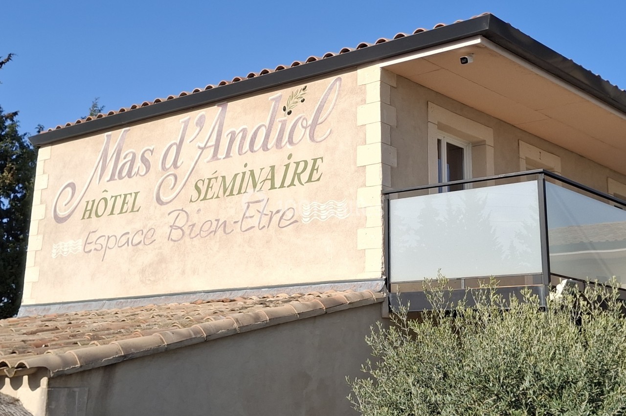 Façade d'un bâtiment avec l'inscription ’Mas d'Andiol, Hôtel Séminaire, Espace Bien-Être’, entouré de végétation.