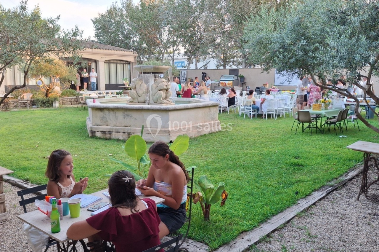 Des personnes profitent d'un jardin avec une fontaine, certaines assises à des tables lors d'un événement en plein air.