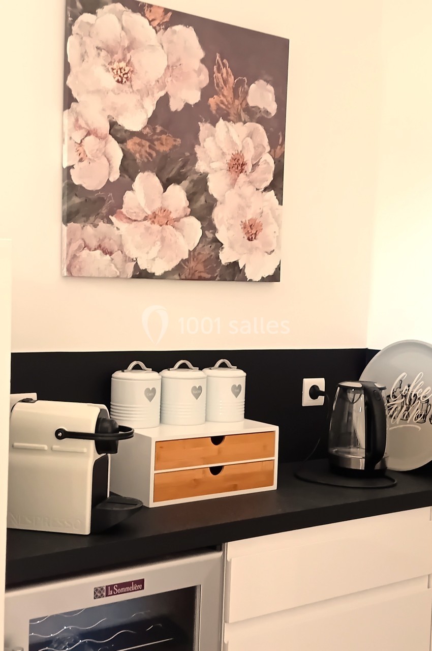 Plan de travail de cuisine avec machine à café, bouilloire, pots de rangement et tableau floral au mur.
