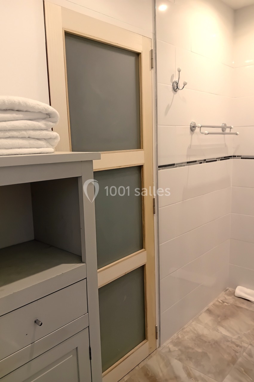 Salle de bain avec porte coulissante en verre dépoli, étagère avec serviettes pliées et douche carrelée blanche.