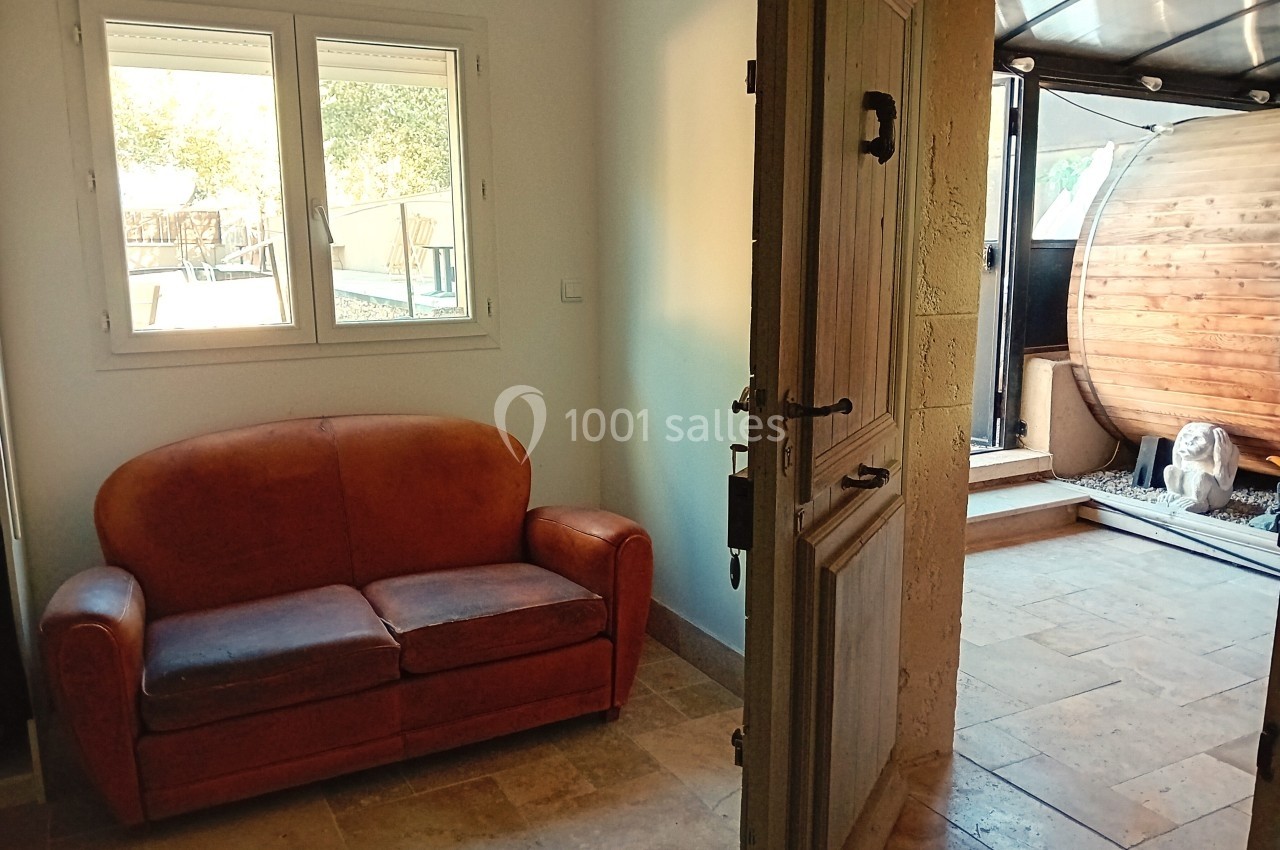 Vue d'une pièce avec un canapé en cuir, une porte ouverte menant à un espace extérieur avec un sauna en bois.