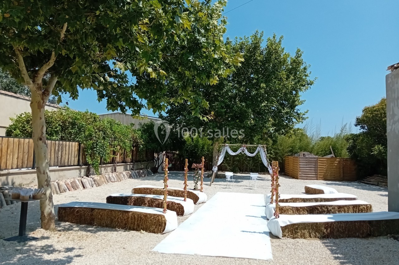 Allée centrale décorée pour une cérémonie en extérieur, entourée de bottes de paille et d'arbres sous un ciel bleu.