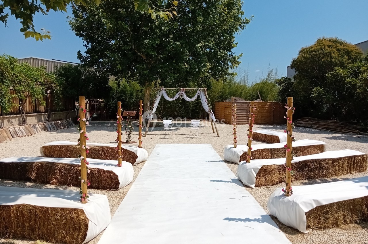 Allée centrale extérieure bordée de bottes de paille recouvertes de tissu blanc, menant à une arche décorée pour une…