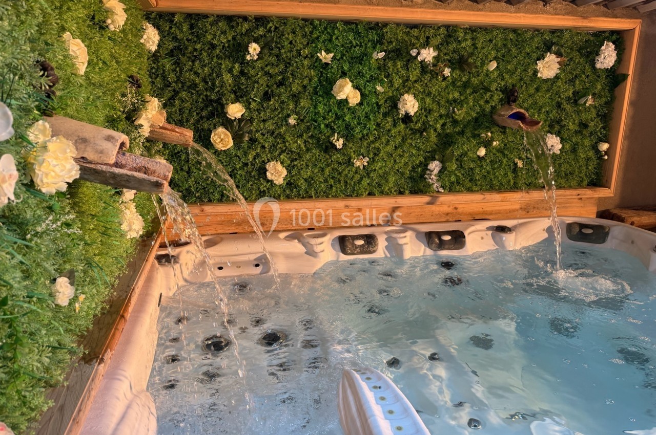 Bain à remous entouré de murs végétalisés avec fleurs blanches et fontaines en bois.