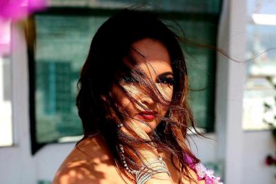 Femme en tenue de danse orientale violette ornée de motifs brillants, posant devant des fleurs et un ciel dégagé.