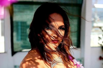 Femme en tenue de danse orientale violette, posant sur une terrasse ensoleillée décorée de plantes et de mobilier extérieur.