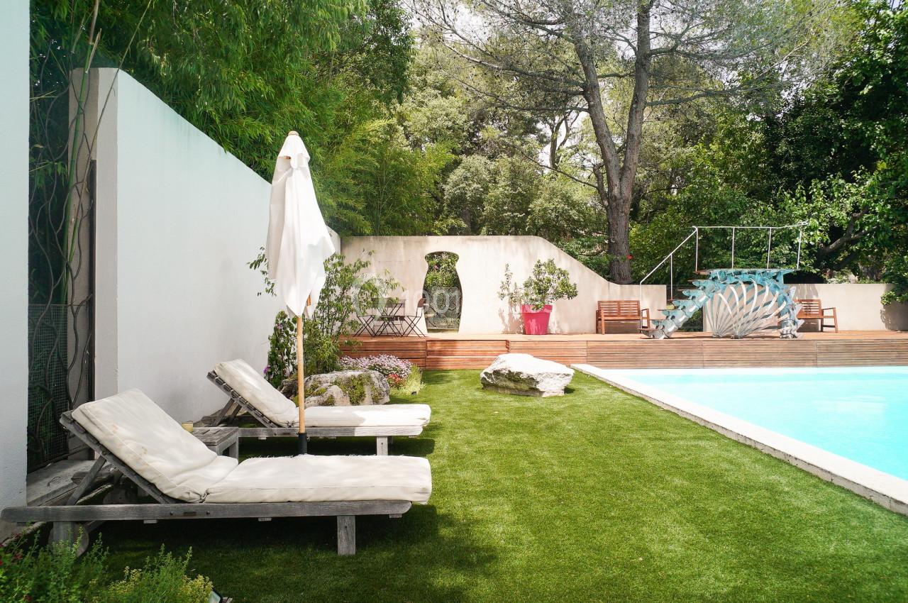 Deux transats et un parasol près d'une piscine entourée de verdure et d'un mur blanc dans un jardin.