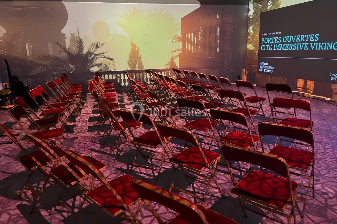 Salle immersive avec rangées de chaises rouges vides, écran affichant ’Portes ouvertes Cité immersive Viking’.