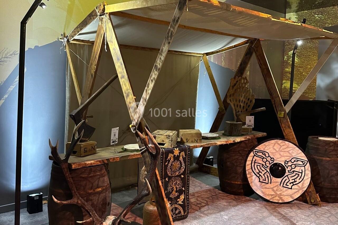 Stand en bois avec une structure en toile, décoré de tonneaux, crânes d'animaux et motifs gravés, dans un espace intérieur.