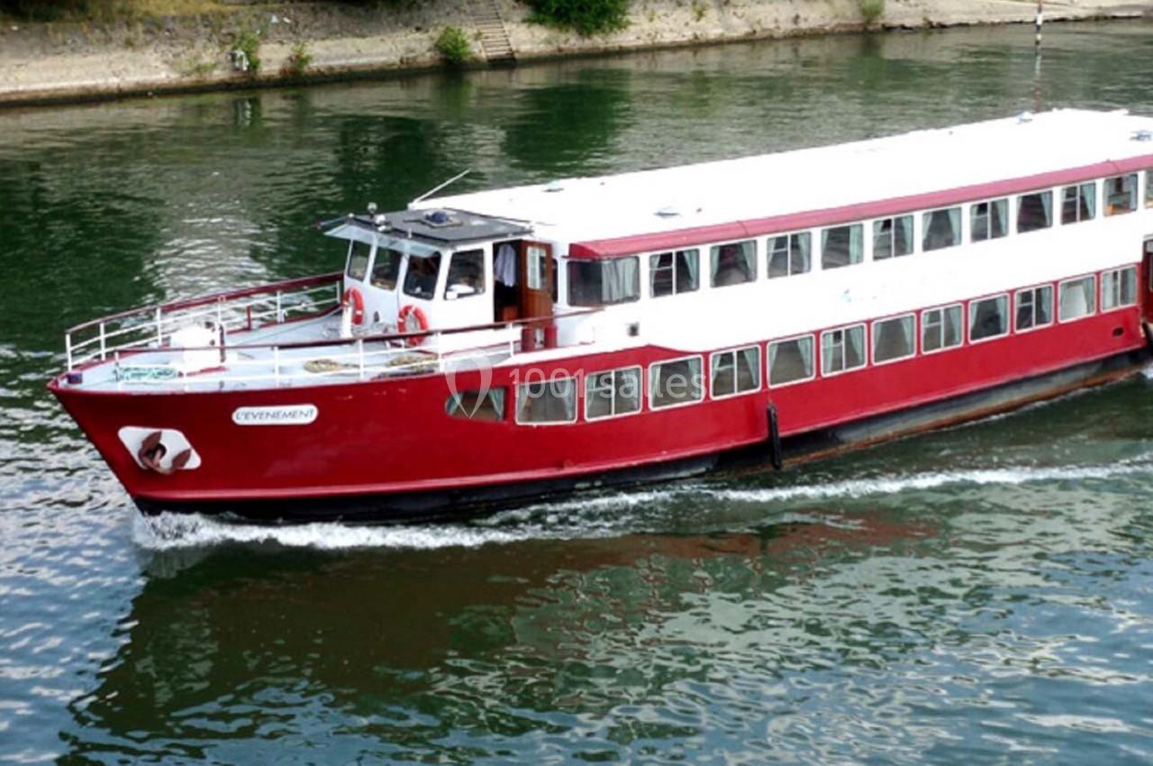 Bateau de croisière rouge et blanc naviguant sur une rivière bordée de végétation.