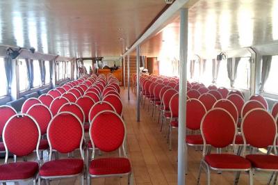 Salle de réception sur un bateau avec des tables dressées, des verres à champagne alignés et une vue sur l'eau en arrière…
