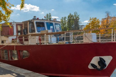 Miniature Location salle Paris 12 (Paris) - La Péniche Croisière de Bercy Corporate #7 Bateau rouge amarré le long d'une berge, entouré d'arbres aux couleurs automnales et sous un ciel dégagé.