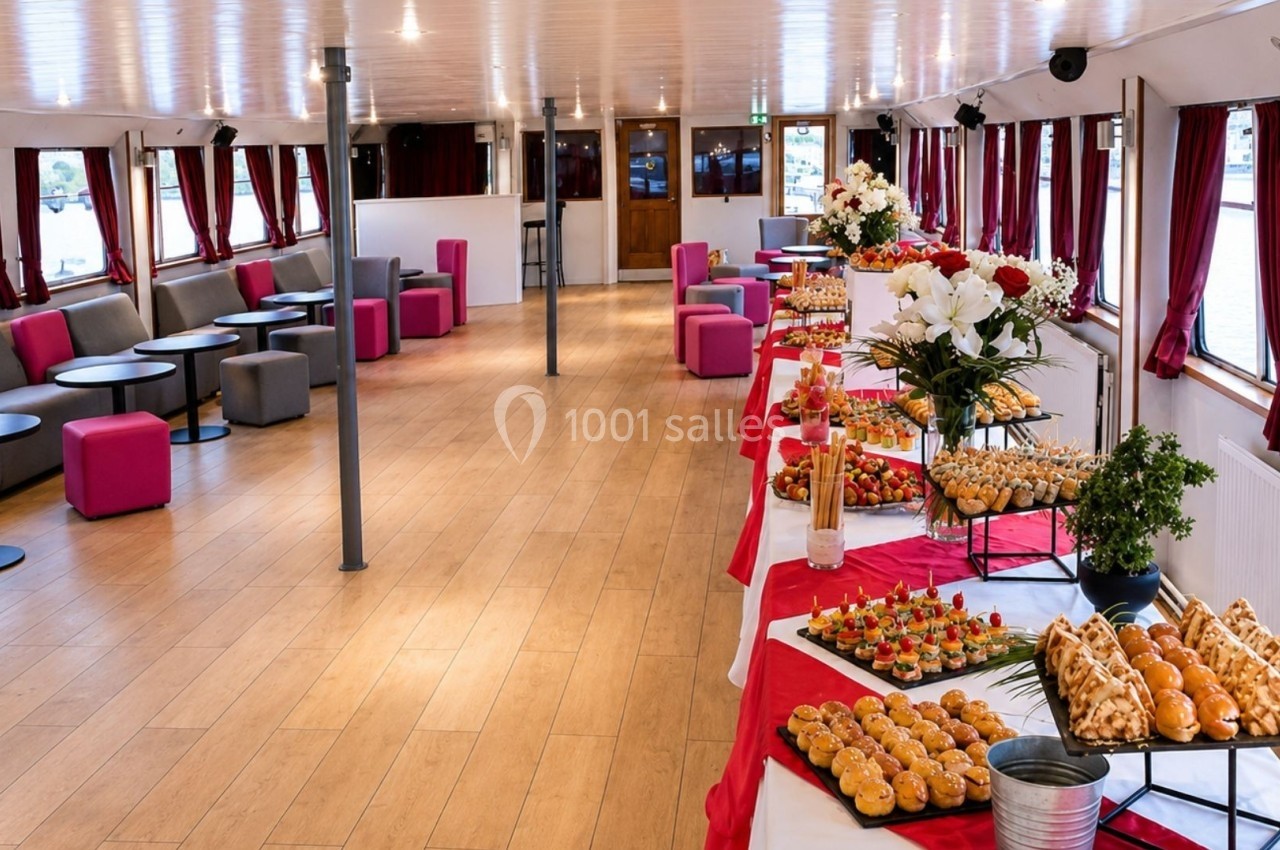 Salle aménagée avec des tables garnies de buffets variés, entourée de banquettes et décorée de rideaux rouges.