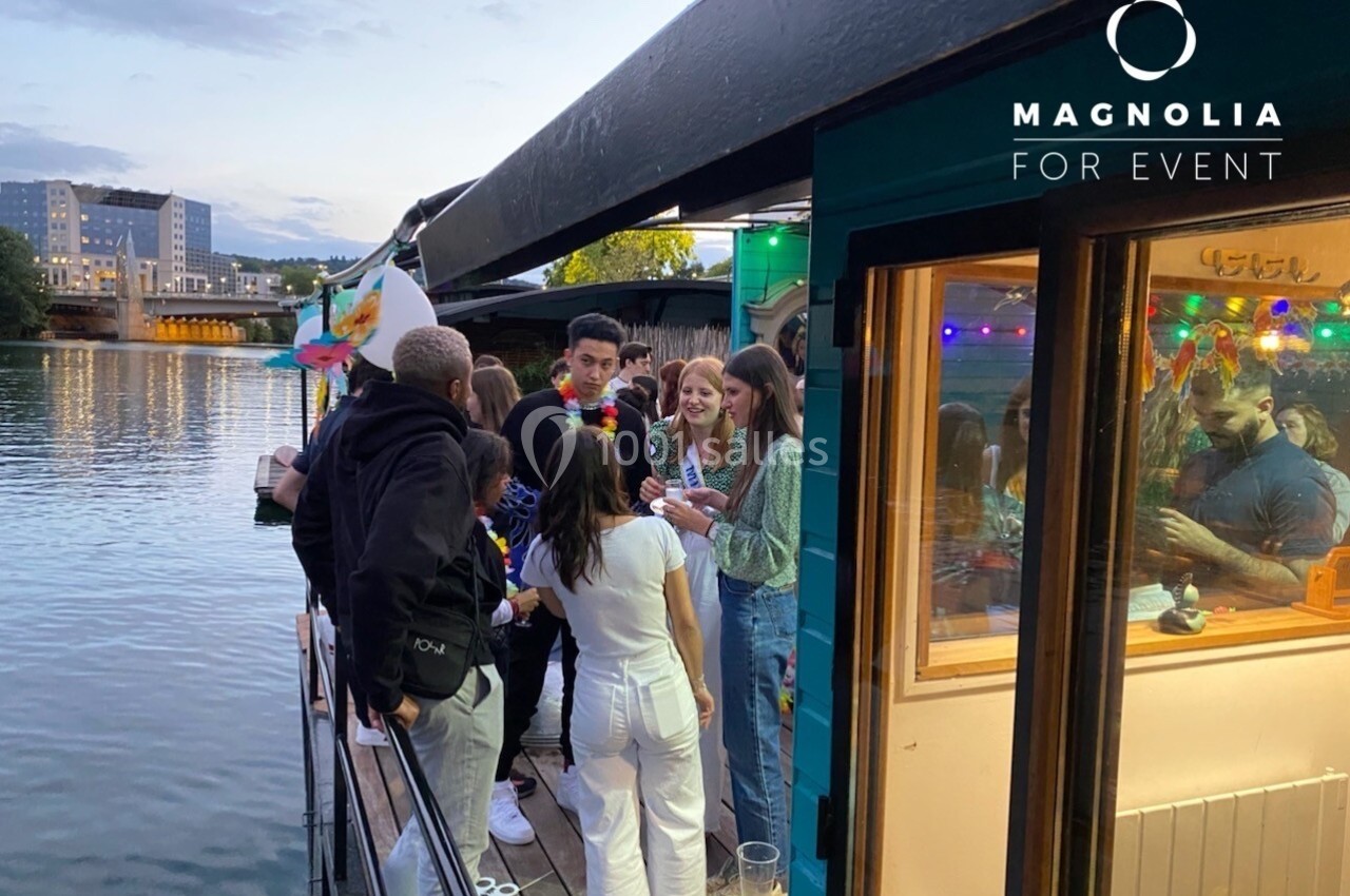 Groupe de personnes discutant et partageant un moment convivial sur la terrasse d'une péniche au bord d'une rivière.