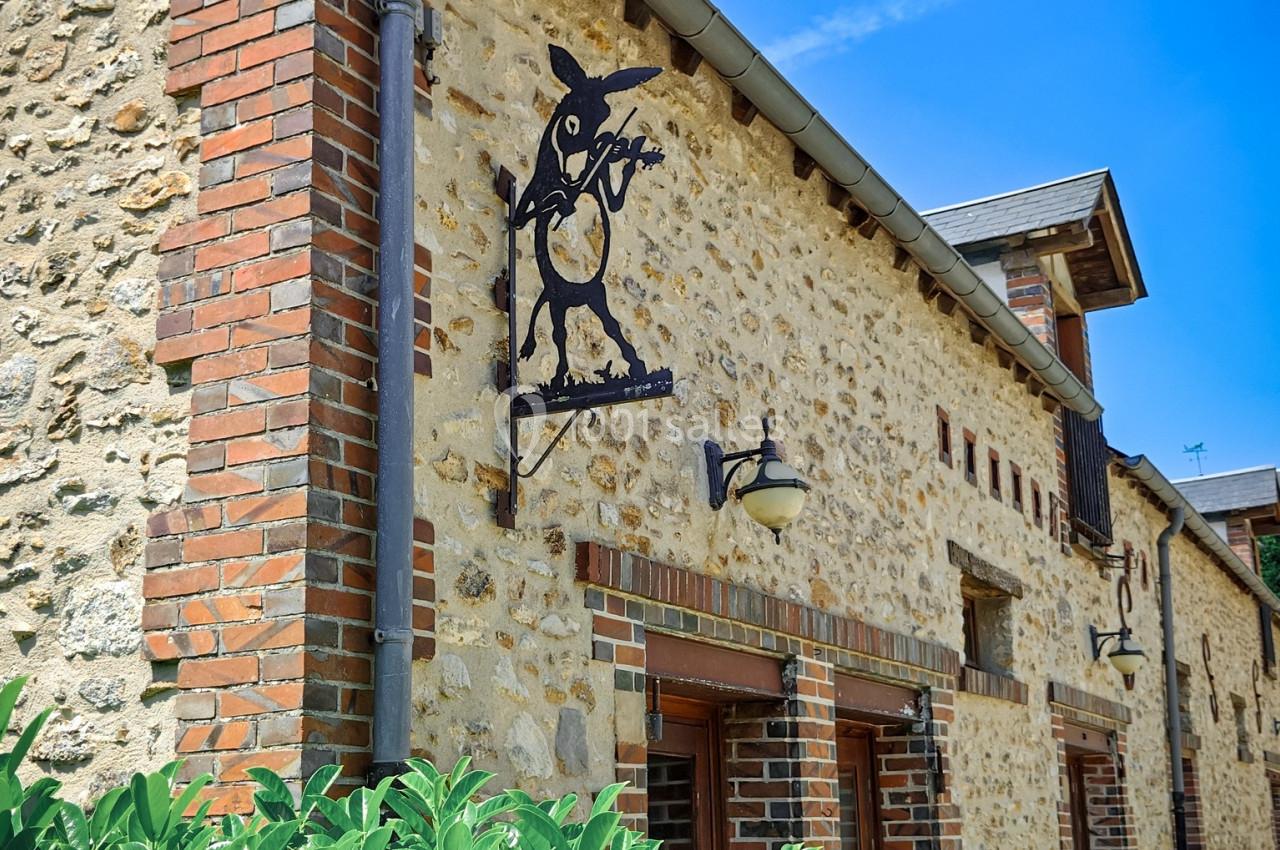 Façade en pierre d'une maison avec enseigne métallique décorative et végétation au premier plan.