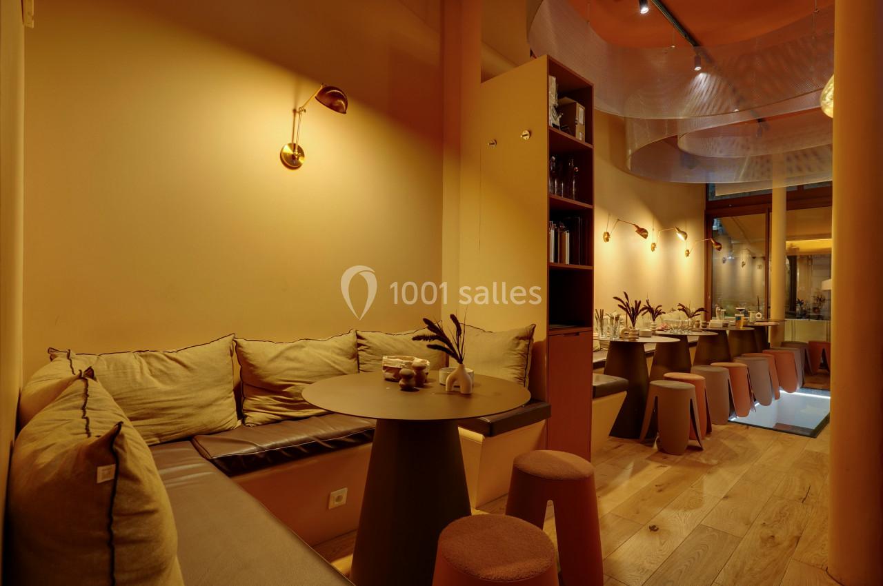 Salle de restaurant chaleureuse avec banquettes, tables rondes, tabourets et éclairage tamisé.