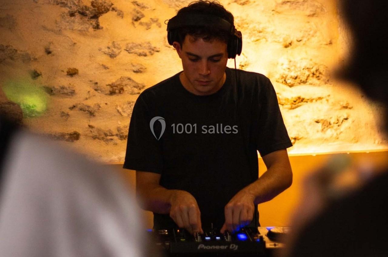 Un DJ mixe de la musique sur une console dans un environnement éclairé de tons chauds avec un mur en pierre en arrière-plan.