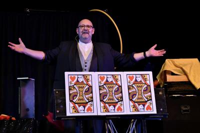 Scène de spectacle avec décorations festives, rideaux noirs, tables couvertes et accessoires colorés sous des éclairages.