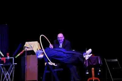 Scène de spectacle avec décorations festives, rideaux noirs, tables ornées et un sapin de Noël illuminé.