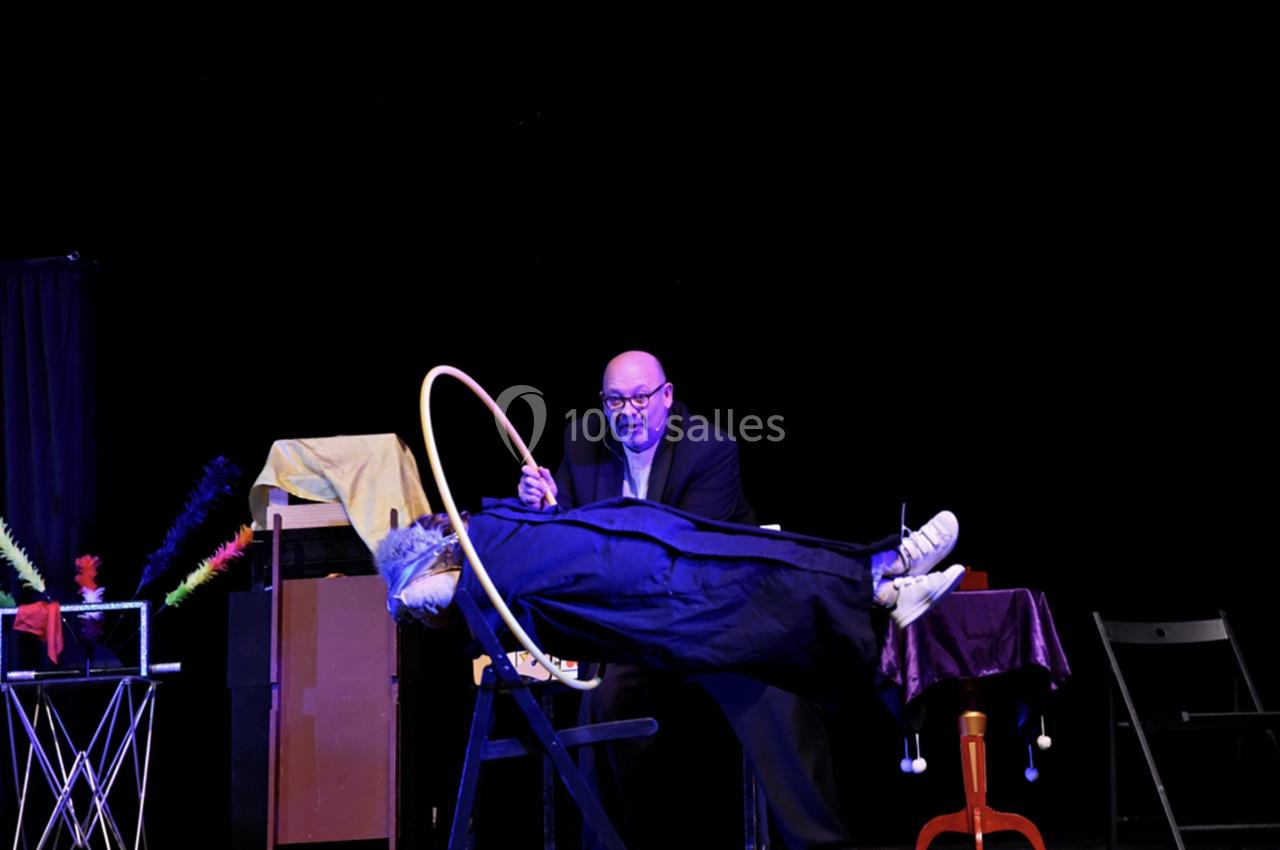 Un magicien fait léviter une personne allongée sur une planche, tenant un cerceau pour montrer l'absence de support.