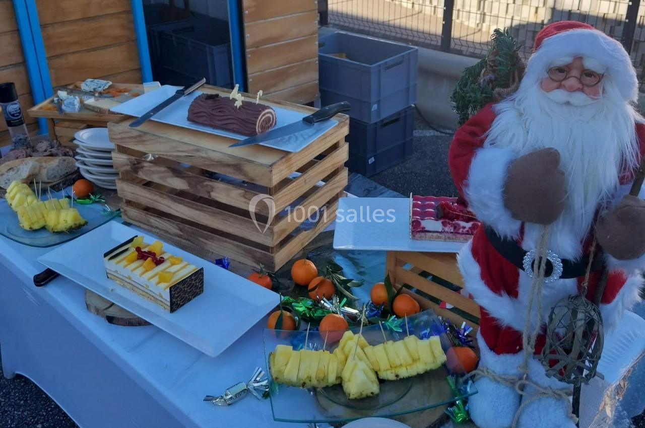 Table garnie de desserts, fruits et bûche de Noël, avec une figurine de Père Noël en décoration.