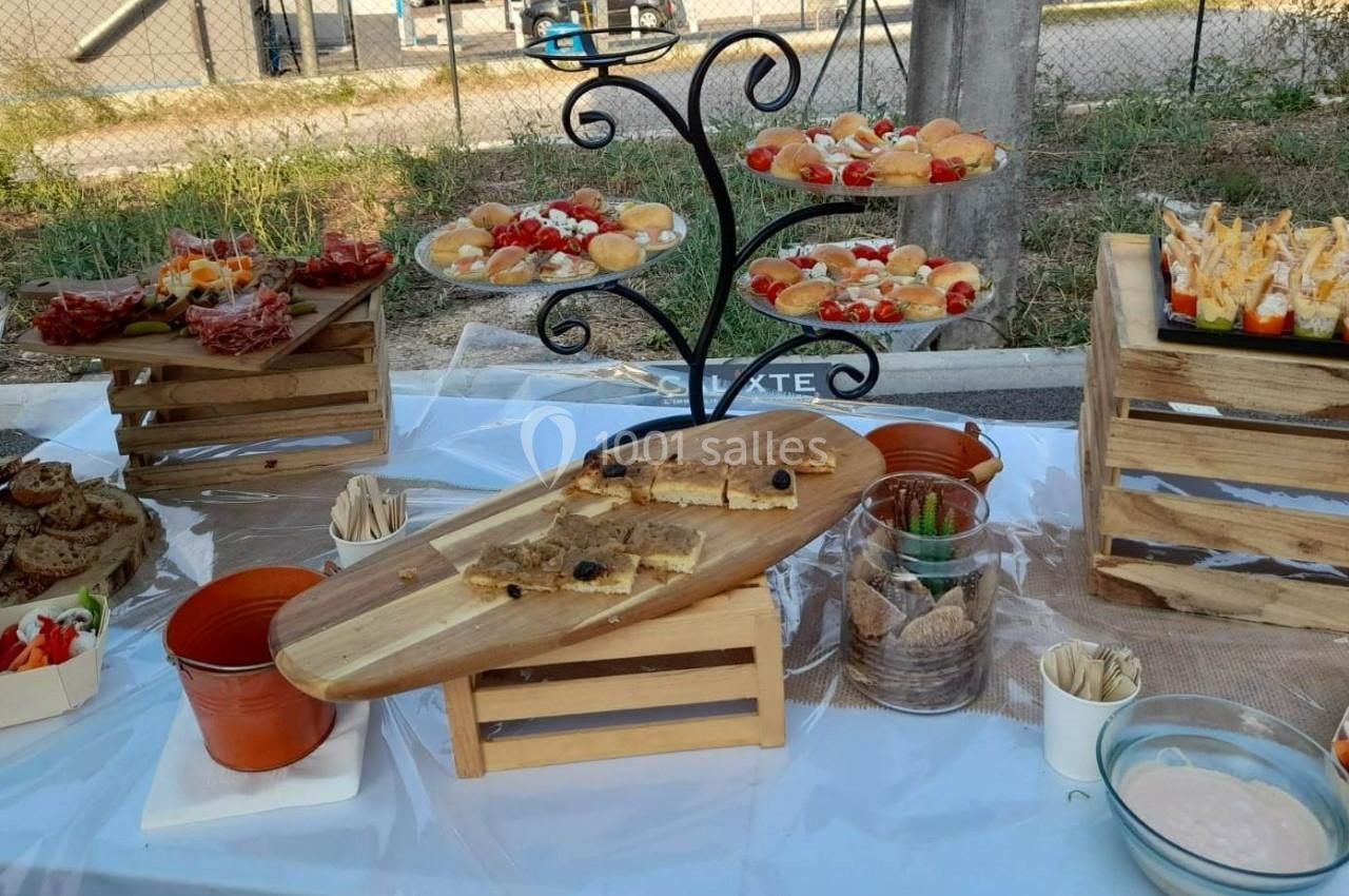 Buffet en extérieur avec divers amuse-bouches, gâteaux, tartes salées et verrines disposés sur des présentoirs en bois.