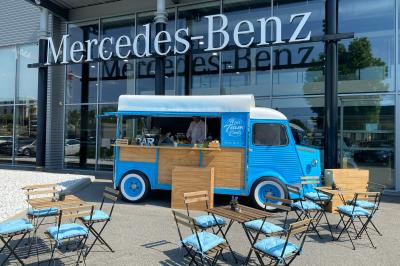 Miniature Traiteur Cannes (Alpes-Maritimes) - Azur Traiteur Events #25 Camion-restaurant bleu vintage devant une concession Mercedes-Benz, avec tables et chaises disposées en terrasse.