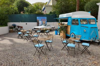 Miniature Traiteur Cannes (Alpes-Maritimes) - Azur Traiteur Events #22 Camion-restaurant bleu vintage devant une concession Mercedes-Benz, avec tables et chaises disposées en terrasse.