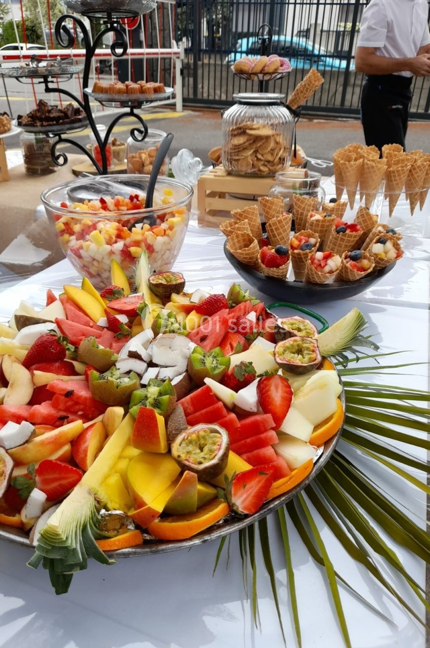 Plateau de fruits frais variés avec salades de fruits, cornets garnis et desserts sur une table extérieure.