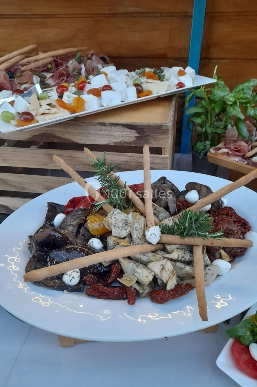 Assiette de légumes grillés, tomates séchées, mozzarella et gressins, avec plateau de charcuterie en arrière-plan.