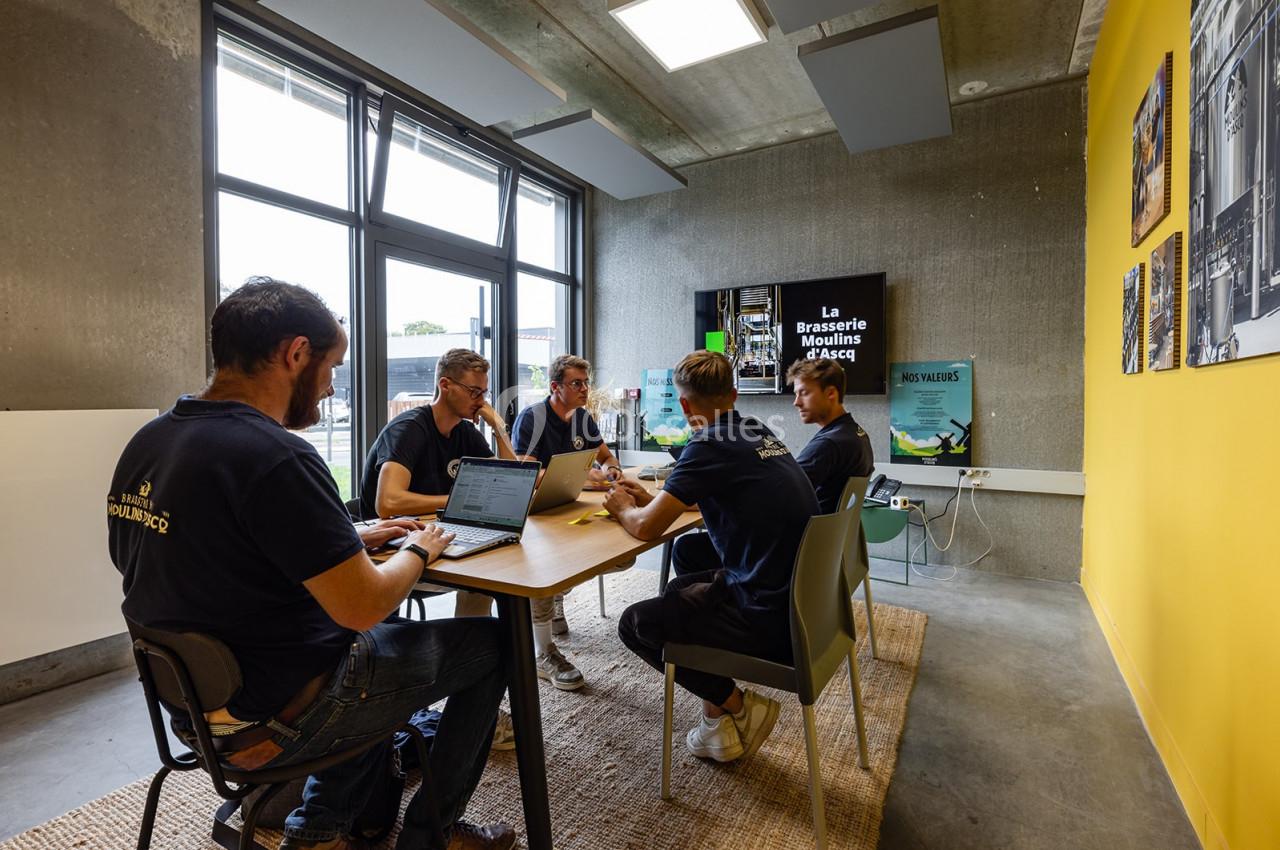 Un groupe de personnes discute autour d'une table dans une salle lumineuse avec des affiches et un écran en arrière-plan.