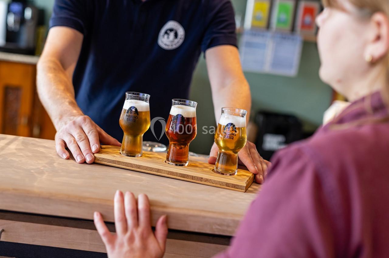 Un serveur présente un plateau en bois avec trois verres de bière différents à une personne au comptoir.