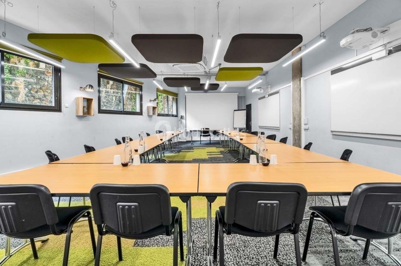 Salle de réunion moderne avec tables en U, chaises noires, éclairage suspendu et grandes fenêtres.