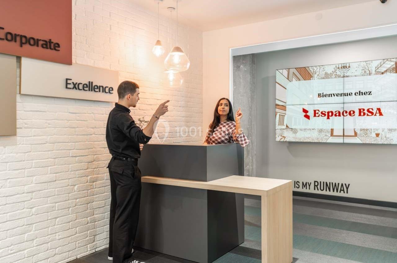 Un homme et une femme discutent à un comptoir d'accueil dans un espace moderne avec un écran affichant ’Espace BSA’.