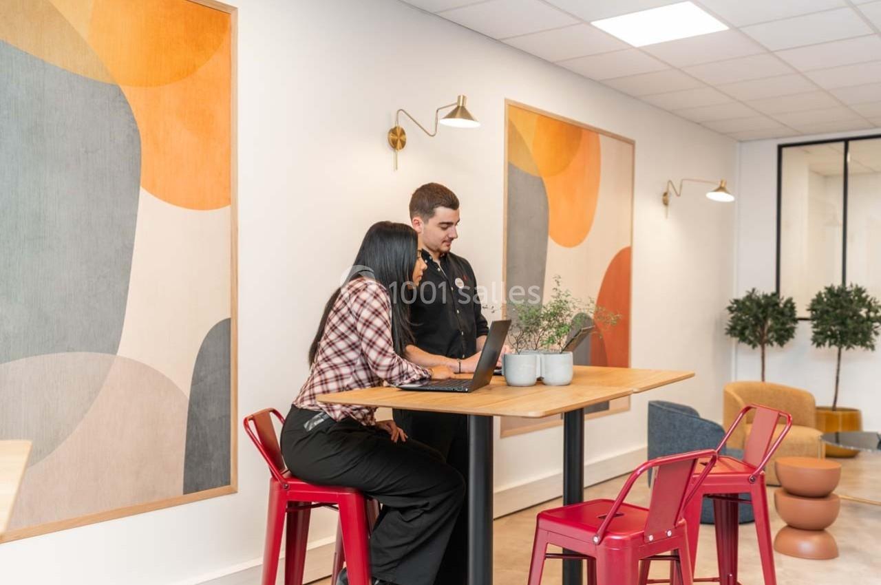 Deux personnes discutent devant un ordinateur portable dans un espace moderne avec des décorations murales colorées.