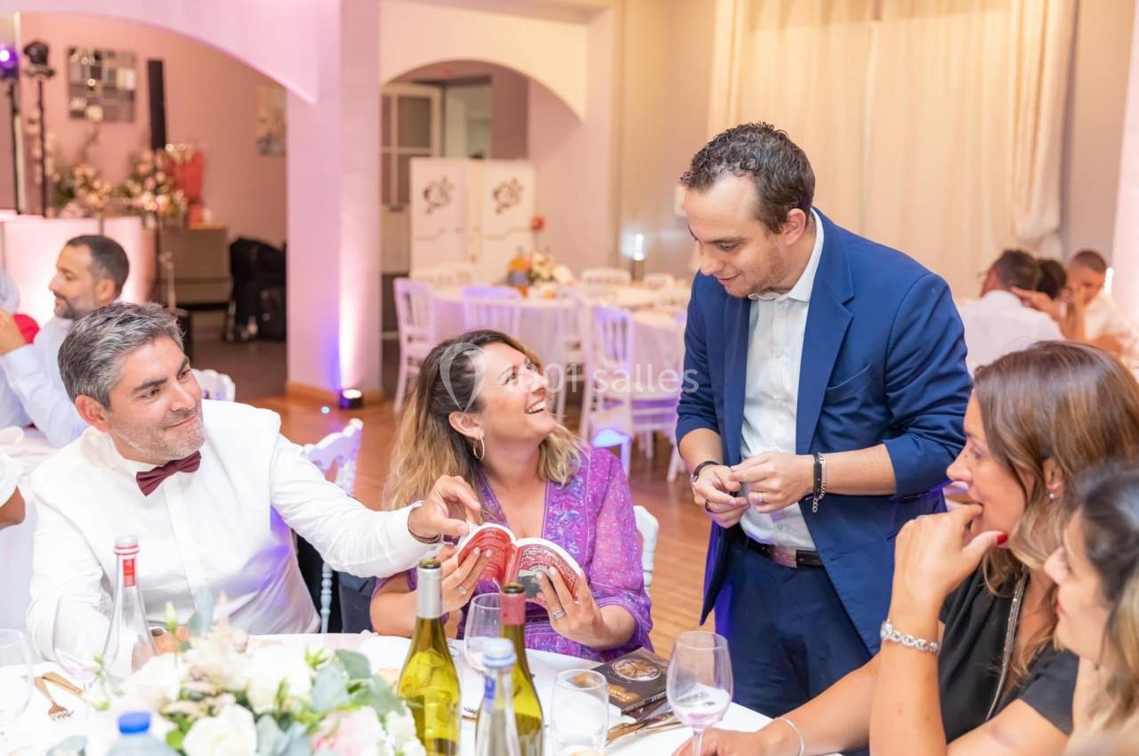 Un magicien réalise un tour de cartes à une table lors d'un événement festif dans une salle décorée.
