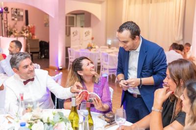 Un groupe de personnes assises autour d'une table, regardant un téléphone, dans un cadre festif avec des fleurs en arrière…