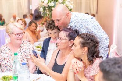 Un groupe de personnes assises autour d'une table, regardant un téléphone, dans un cadre festif avec des fleurs en arrière…