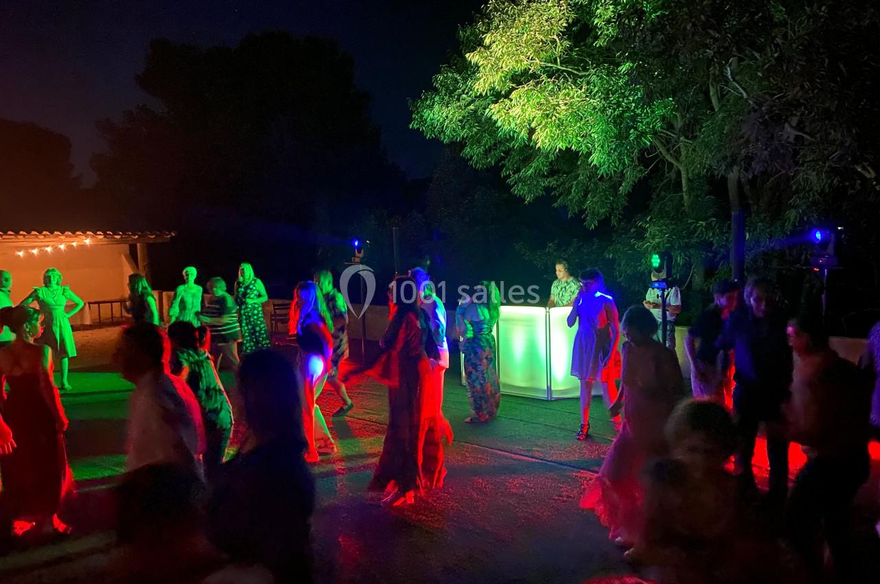 Personnes dansant en extérieur la nuit, éclairées par des lumières colorées près d'une piste et d'un stand lumineux.