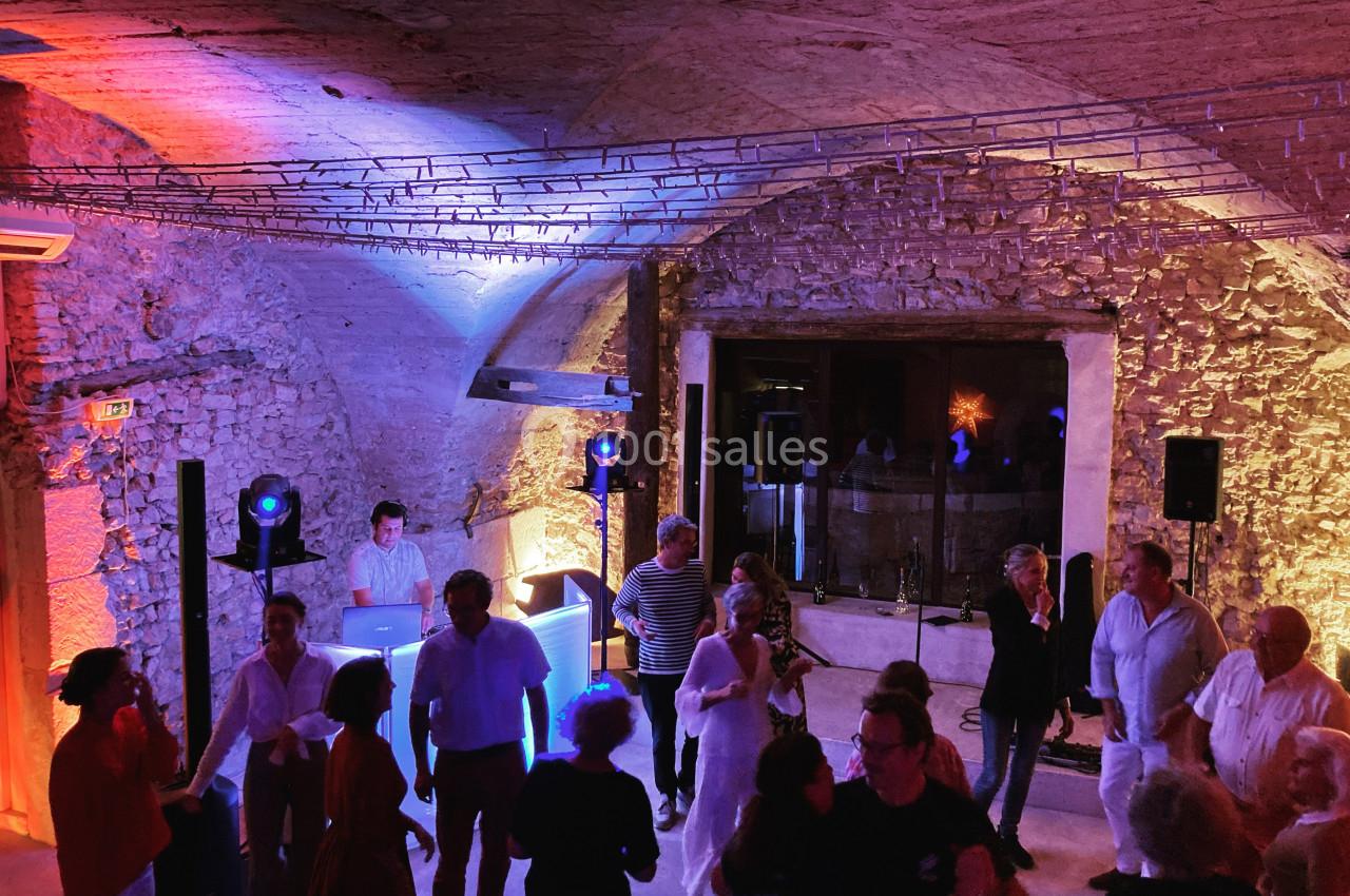 Personnes dansant dans une salle voûtée en pierre, éclairée par des lumières colorées, avec un DJ en arrière-plan.