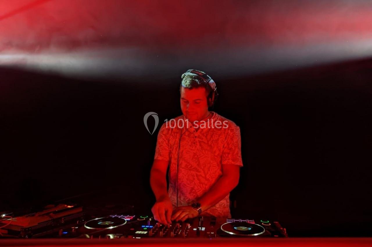Un DJ mixe de la musique sur une table de mixage sous un éclairage rouge dans une ambiance sombre.