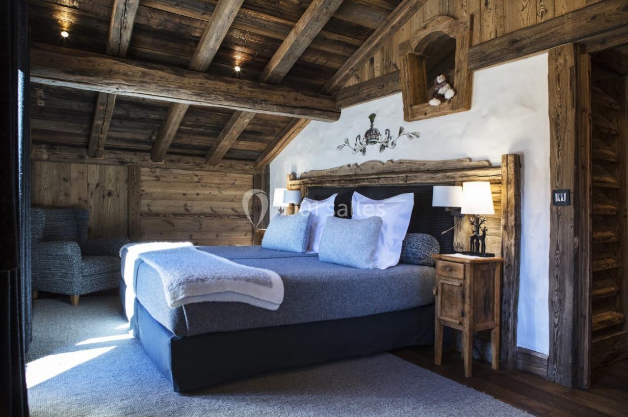 Chambre rustique avec poutres apparentes, lit double, tables de chevet en bois et éclairage doux.