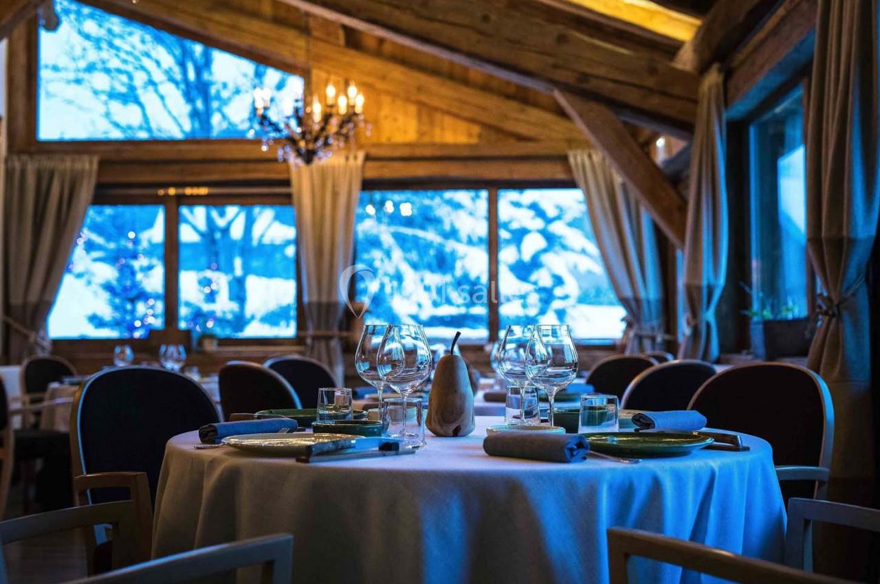 Salle de restaurant chaleureuse avec tables dressées, grandes baies vitrées et vue sur un paysage enneigé.