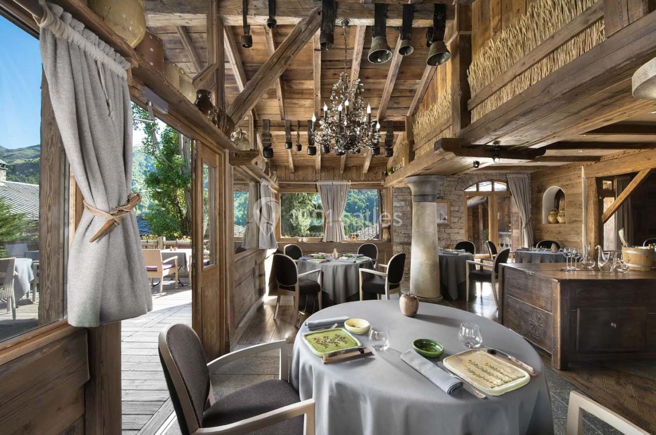 Salle de restaurant en bois avec grandes baies vitrées, tables dressées et vue sur un paysage montagneux.
