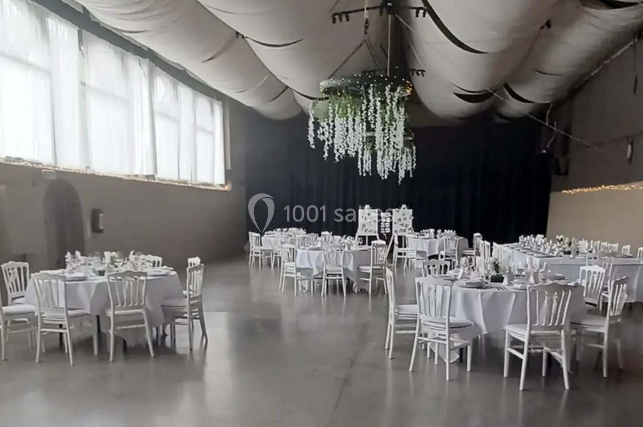Salle de réception décorée avec des tables rondes dressées, des chaises blanches et un plafond orné de guirlandes suspendues.