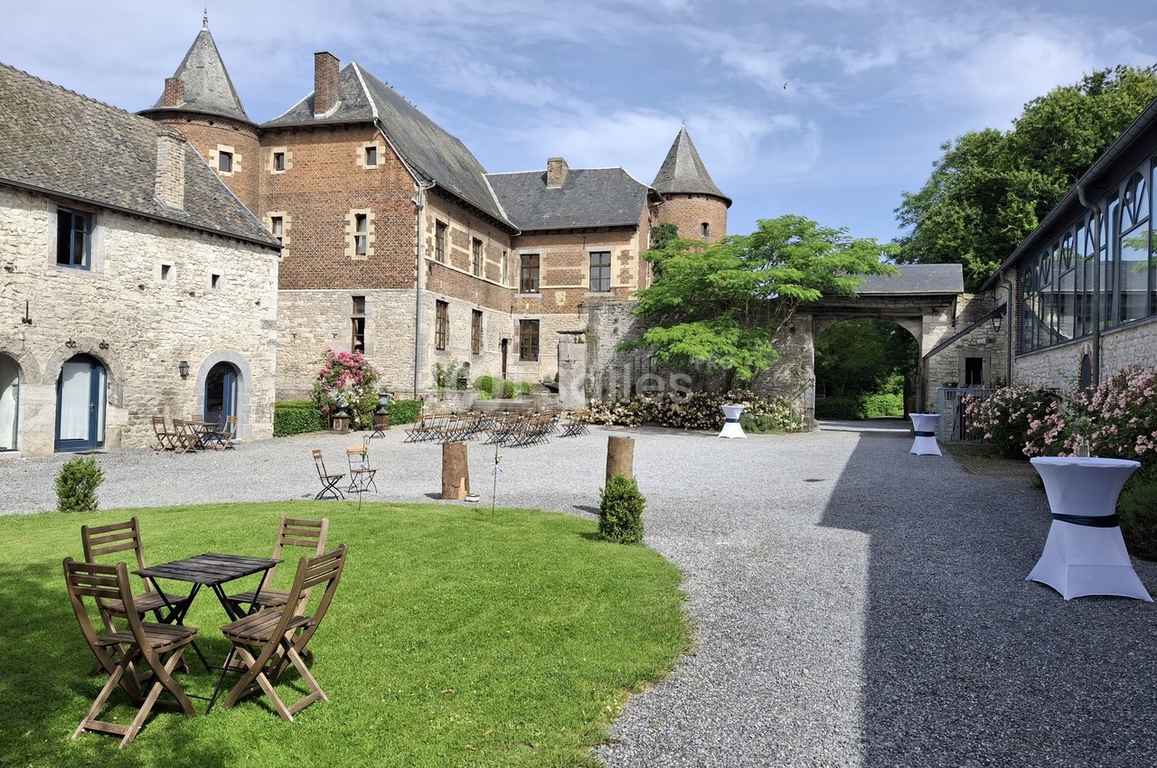 Cour d'un château historique avec pelouse, mobilier de jardin en bois, allées gravillonnées et bâtiments en pierre.