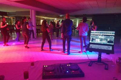 Un homme s'exprime au micro devant un public rassemblé dans une cour extérieure entourée de végétation.