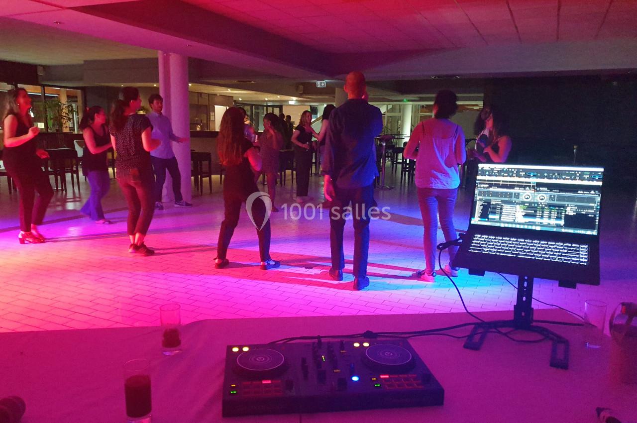 Des personnes dansent en groupe sous des lumières colorées, avec une table de mixage et un écran au premier plan.