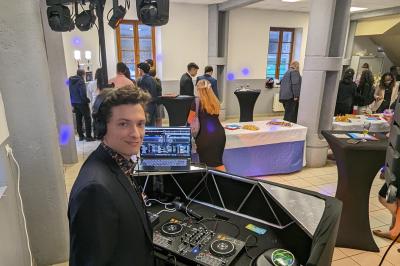 Un homme s'exprime au micro devant un public rassemblé dans une cour extérieure entourée de végétation.