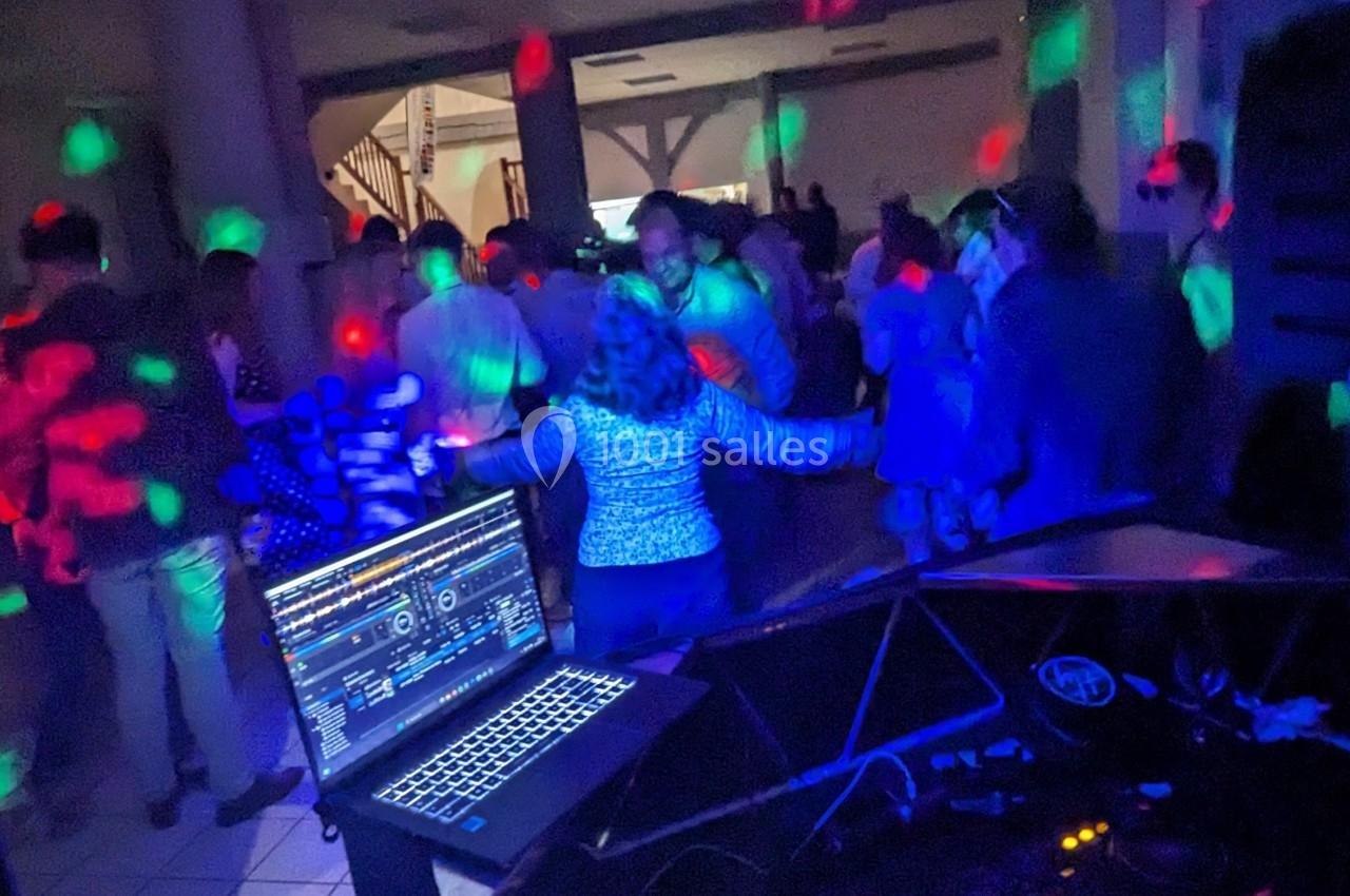 Personnes dansant dans une salle sombre éclairée par des lumières colorées, avec un ordinateur de DJ au premier plan.